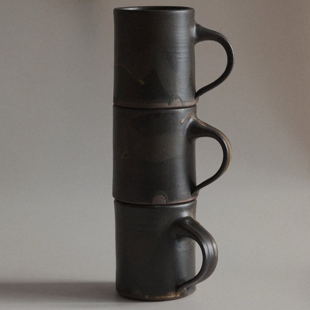 Stack of three black ceramic mugs on a gray background