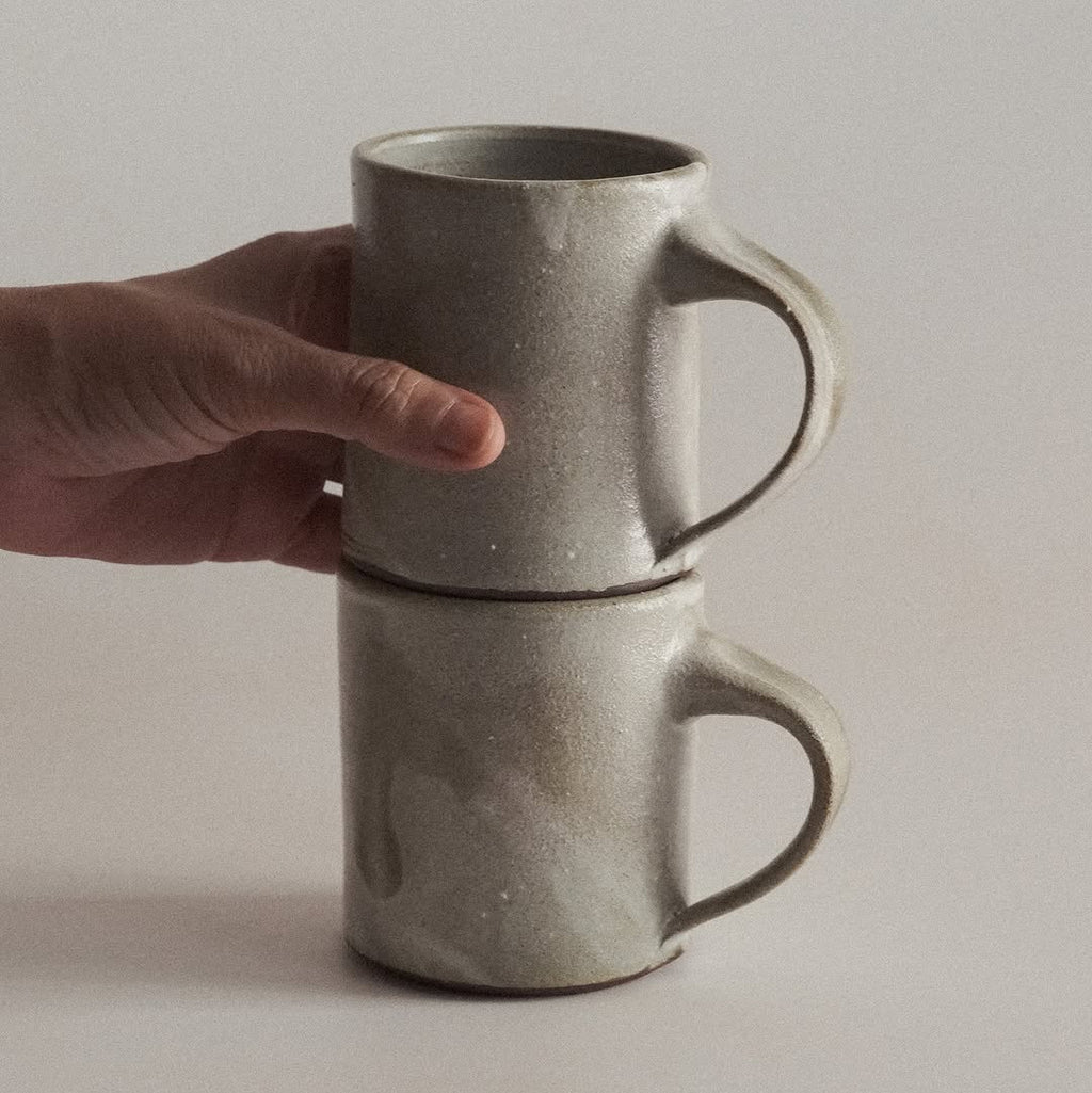Hand holding two stacked ceramic mugs against a plain background